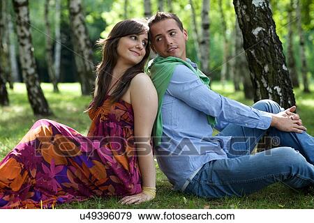 Stock Photo - Young couple sitting back to back in park. Fotosearch