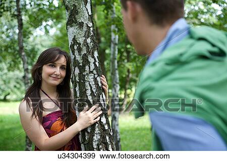 Stock Photo - Young couple standing in park by tree trunk. Fotosearch
