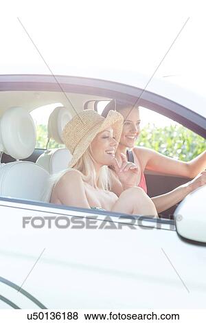 Young female friends enjoying road trip in car on sunny day View Large Photo Image Stock Photo - Young female friends enjoying road trip in car on sunny day. Fotosearch
