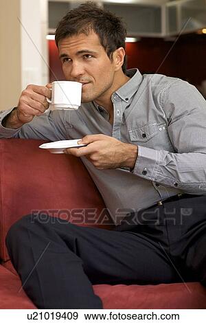 Young man drinking tea, sitting in sofa View Large Photo Image Stock Photo - Young man drinking tea, sitting in sofa. Fotosearch