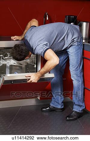 Young man looking at dish washer View Large Photo Image Stock Image - Young man looking at dish washer. Fotosearch