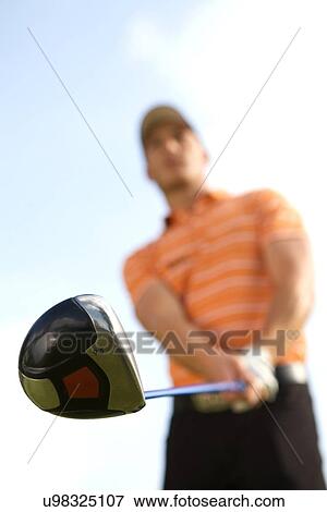 Stock Photo - Young man playing golf, low angle view. Fotosearch