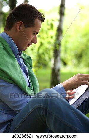 Young man reading book in park View Large Photo Image Stock Image - Young man reading book in park. Fotosearch