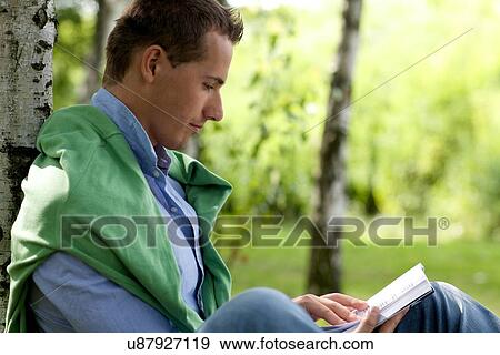 Stock Photo - Young man reading book in park. Fotosearch