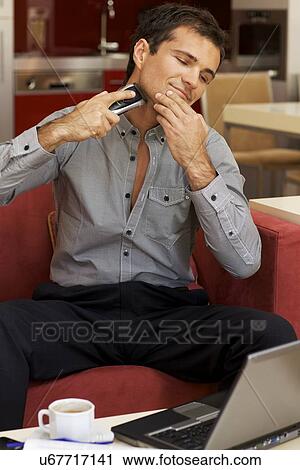 Stock Image - Young man shaving with electric shaver. Fotosearch