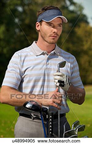 Stock Photography - Young man standing by golf bag full of sticks. Fotosearch