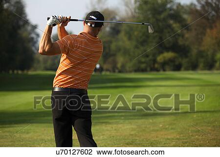 Stock Image - Young man swinging golf club, rear view. Fotosearch