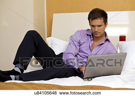 Stock Photo - Young man using laptop on bed. Fotosearch