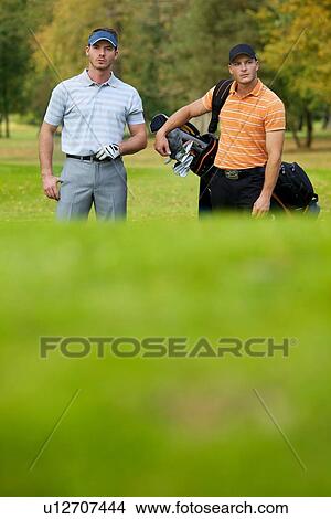 Young men standing on golf course carrying bags View Large Photo Image Picture - Young men standing on golf course carrying bags. Fotosearch