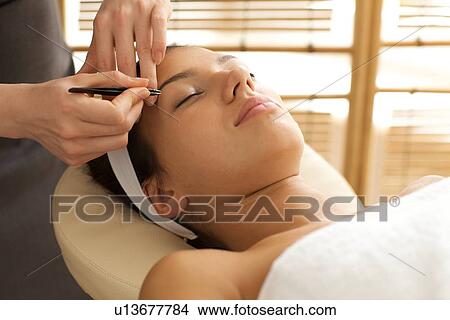 Picture - Young woman having eye-brows plucked. Fotosearch