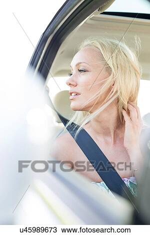 Stock Image - Young woman looking through car window. Fotosearch