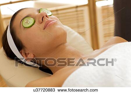 Young woman lying down in massage table with cucumbers on eyes View Large Photo Image Stock Image - Young woman lying down in massage table with cucumbers on eyes. Fotosearch