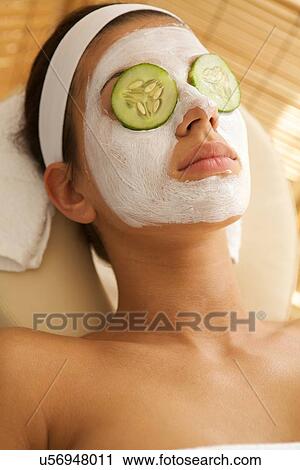 Young woman lying down on massage table with cucumbers on eyes View Large Photo Image Stock Image - Young woman lying down on massage table with cucumbers on eyes. Fotosearch