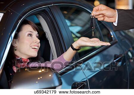 Stock Photo - Young woman receiving the car keys from car salesman. Fotosearch