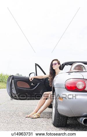 Young woman sitting in convertible on country road against clear sky View Large Photo Image Stock Image - Young woman sitting in convertible on country road against clear sky. Fotosearch