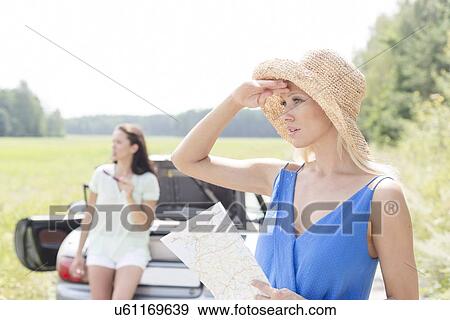Young woman with map looking away while friend leaning on convertible in background View Large Photo Image Stock Photo - Young woman with map looking away while friend leaning on convertible in background. Fotosearch
