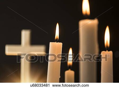 Stock Image - Burning candles with cross in background. Fotosearch