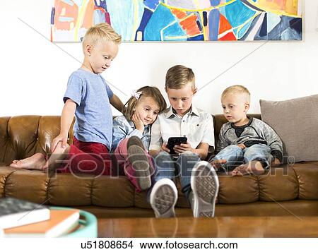 Picture - Children (2-3, 4-5, 6-7) sitting on sofa and using smartphone. Fotosearch
