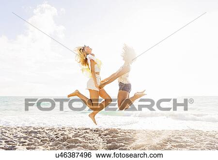 Stock Photograph - Female friends jumping on beach. Fotosearch