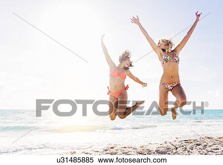 Stock Photography - Female friends jumping on beach. Fotosearch