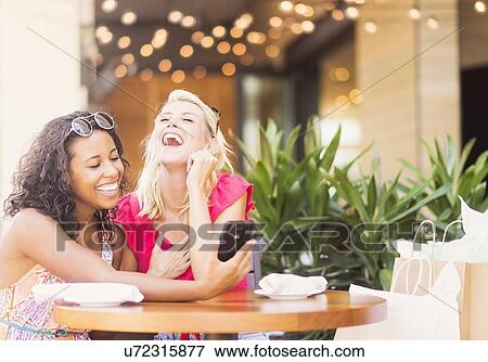 Female friends using smart phone in cafe View Large Photo Image Stock Photo - Female friends using smart phone in cafe. Fotosearch