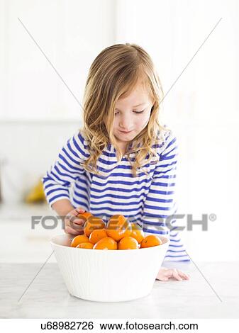 Stock Photograph - Girl (4-5) looking at oranges, smiling. Fotosearch