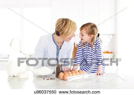 Stock Image - Girl (4-5) talking with mom in kitchen. Fotosearch