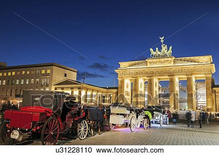 Stock Image - Horse carts in front of illuminated Brandenburg Gate. Fotosearch