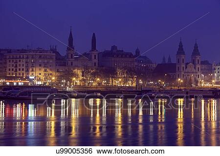 Stock Photograph - Illuminated waterfront and reflections in river. Fotosearch