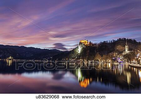 Stock Photo - Lake Bled and illuminated Church of the Assumption reflecting in lake. Fotosearch
