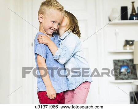 Stock Photograph - Little girl (4-5) whispering into brother's (4-5) ear. Fotosearch
