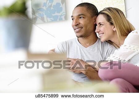 Stock Photo - Mid adult couple embracing in living room. Fotosearch