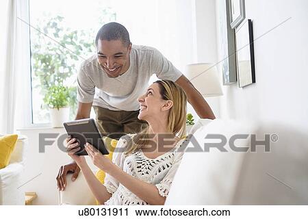 Mid adult couple looking at digital tablet in living room View Large Photo Image Stock Image - Mid adult couple looking at digital tablet in living room. Fotosearch