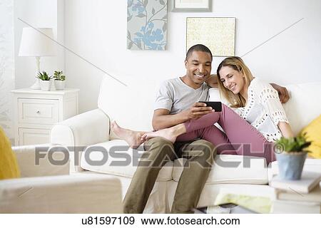 Mid adult couple looking at smart phone in living room View Large Photo Image Stock Photo - Mid adult couple looking at smart phone in living room. Fotosearch