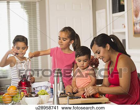 Stock Image - Mother and children (2-3, 6-7, 8-9) preparing fruit cocktails. Fotosearch