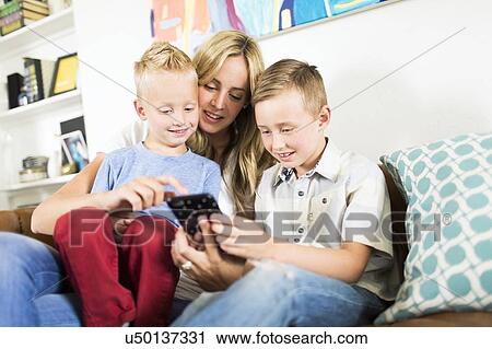 Stock Image - Mother with children (4-5, 6-7) using smartphone on sofa. Fotosearch