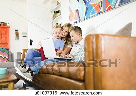 Stock Photograph - Mother with children (4-5, 6-7) using laptop on sofa. Fotosearch