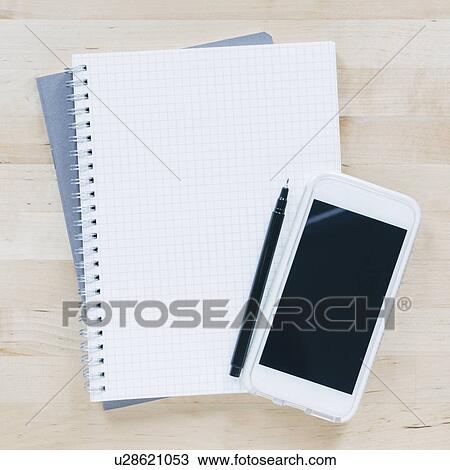 Stock Image - Overhead view of pen and smart phone on notebook. Fotosearch