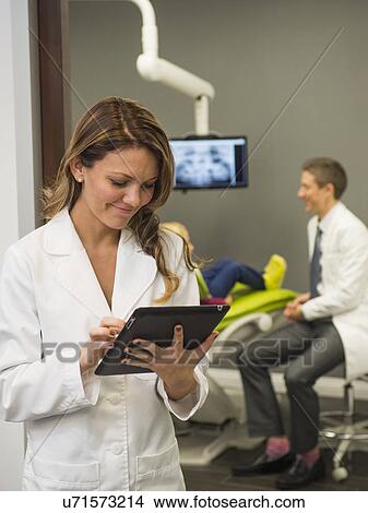 Portrait of dentist with colleague and patient (8-9) in background View Large Photo Image Picture - Portrait of dentist with colleague and patient (8-9) in background. Fotosearch