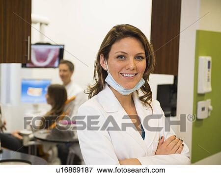 Stock Photo - Portrait of dentist with colleague and patient in background. Fotosearch