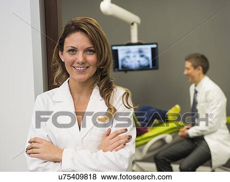 Stock Photo - Portrait of dentist with colleague and patient (8-9) in background. Fotosearch