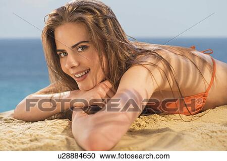 Stock Image - Portrait of young woman lying on beach. Fotosearch