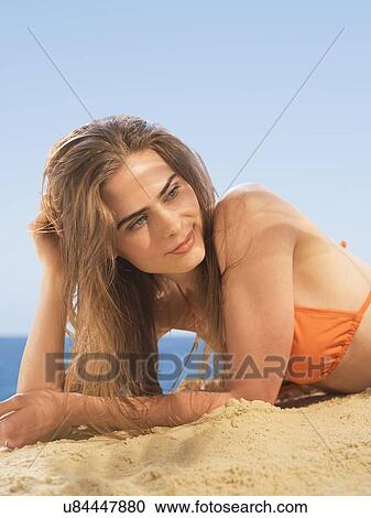 Stock Image - Portrait of young woman lying on beach. Fotosearch