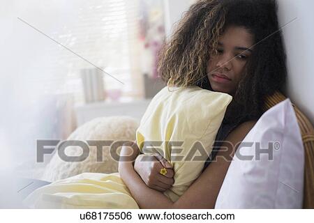 Stock Photograph - Teenage girl (14-15) sitting on bed, embracing pillow. Fotosearch