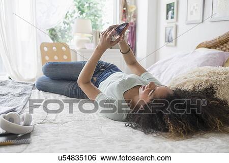 Stock Photograph - Teenage girl (16-17) texting in bedroom. Fotosearch