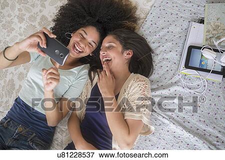 Stock Photo - Teenage girls (14-15, 16-17) texting in bedroom. Fotosearch