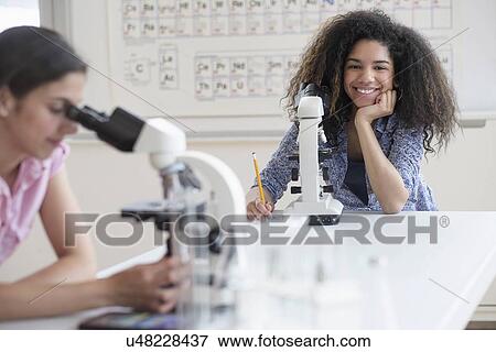 Stock Photo - Teenage girls (14-15, 16-17) using microscope in science class. Fotosearch