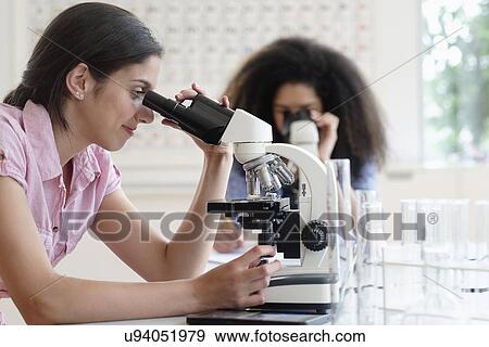 Stock Photo - Teenage girls (14-15, 16-17) using microscope in science class. Fotosearch