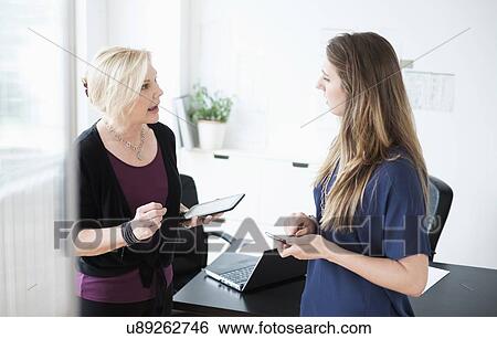 Two women talking in office View Large Photo Image Stock Photograph - Two women talking in office. Fotosearch