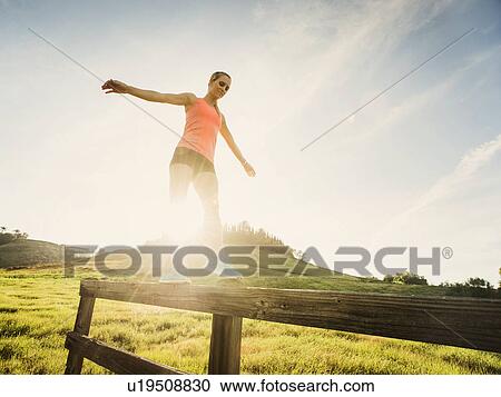 Stock Image - Woman balancing on wooden fence. Fotosearch